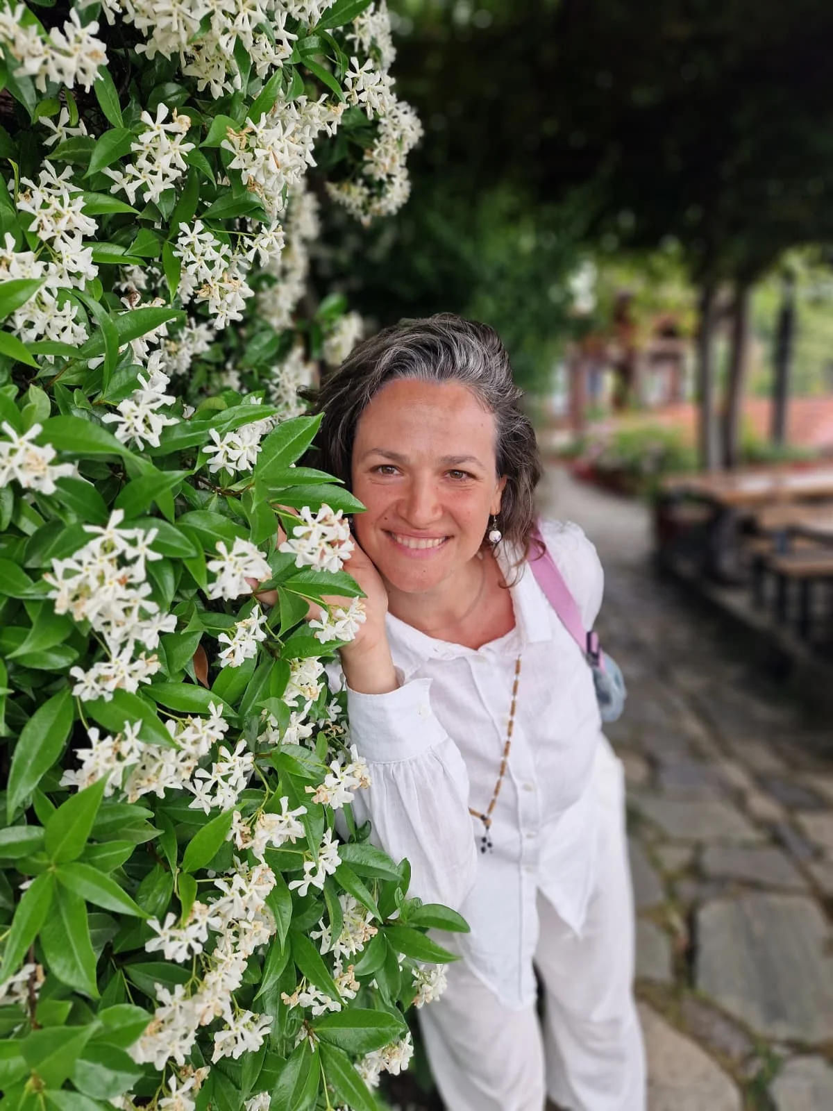 Teodora Haidu zâmbește lângă o plantă cu flori albe